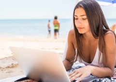 Beautiful woman working online on laptop while lying on beach under sun umbrella near sea. Happy smiling freelancer girl relaxing and using notebook for freelance internet work. Beautiful woman working online on laptop while lying on beach under sun umbrella near sea. Happy smiling freelancer girl relaxing and using notebook for Ffeelance internet work.